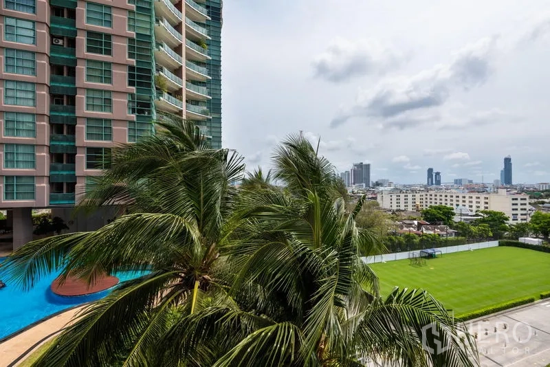 คอนโด ให้เช่าในBang Kho Laem, Bangkok - อาคารคอนโดพร้อมระเบียงกระจกสีเขียว สระว่ายน้ำทรงโค้ง ต้นปาล์ม และวิวสกายไลน์กรุงเทพเหนือสนามหญ้า