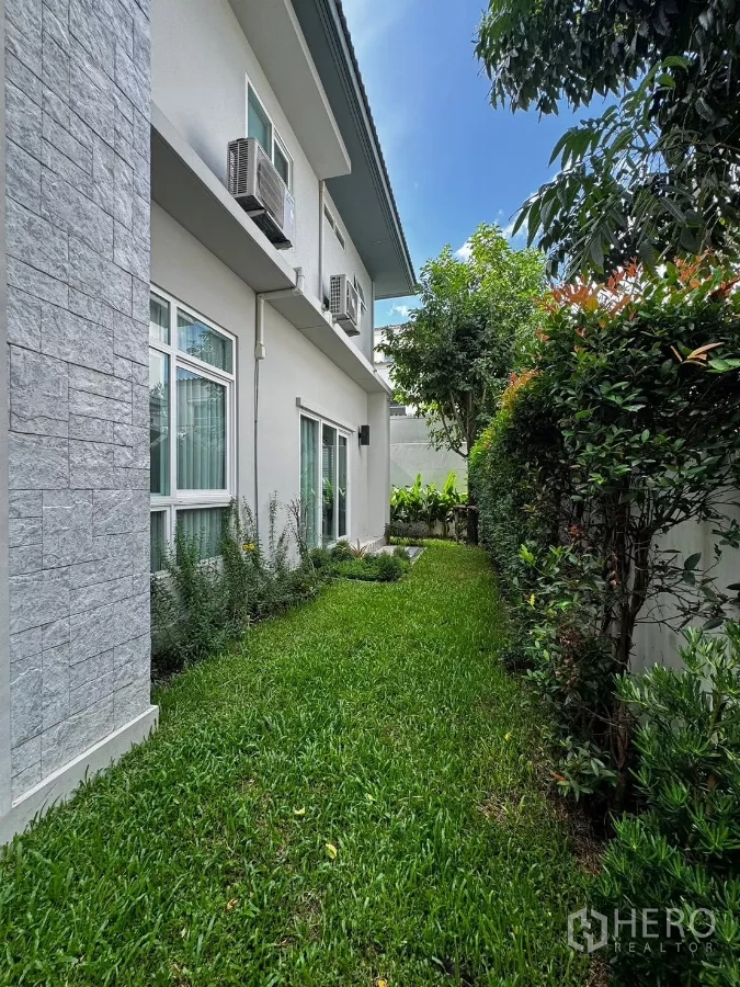 บ้าน ให้เช่าในPrawet, Bangkok - สนามหญ้าด้านข้างตัวบ้านสองชั้น มีประตูบานเลื่อนและคอยล์แอร์ภายนอก.