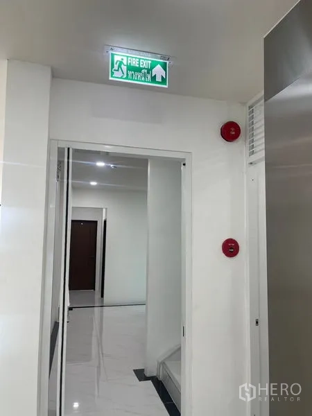 Home Office for rent or sale in Wang Thonglang, Bangkok - Hallway with fire exit sign, alarms and white tiled floors.