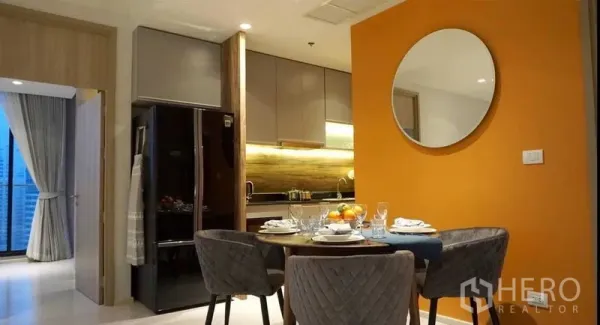Condominium for rent in Pathum Wan, Bangkok - Open kitchen and dining area with orange accent wall, round mirror and table set for four.