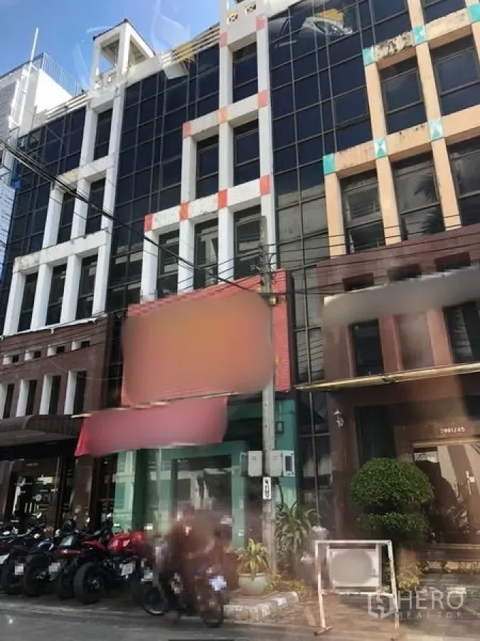Office Space for sale in Bang Kapi, Bangkok - Facade of a mid-rise commercial building with glass windows and street-front shops and motorbike parking.