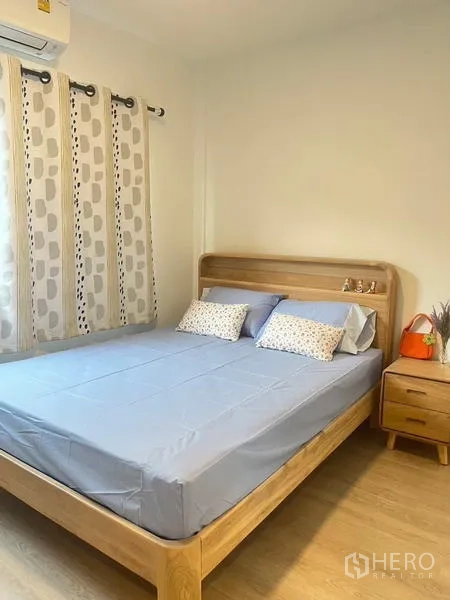 联排别墅 出租在Prawet, Bangkok - 明亮卧室，木质床架、床头柜与空调，窗口采光佳。