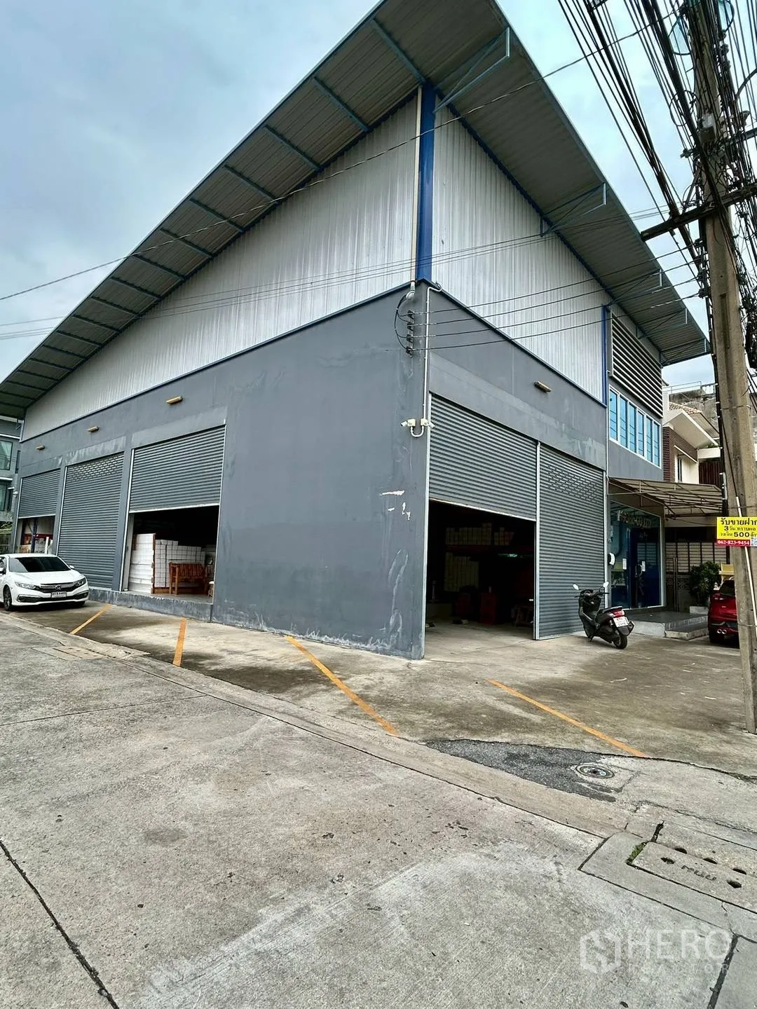Warehouse for rent in Suan Luang, Bangkok - Corner exterior of the warehouse showing several rolling doors and parking lines.