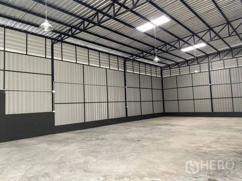 Warehouse for rent in Wang Thonglang, Bangkok - Open warehouse bay showing metal panel walls, hanging industrial lights and wide column-free space.
