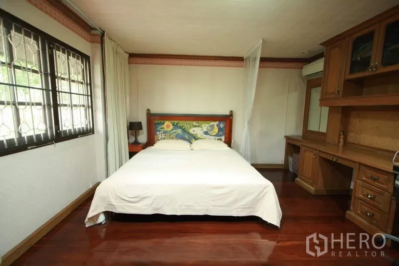 Detached House for rent in Bang Phli, Samut Prakan - Bedroom with wood floors, window security grills and a long built-in desk and wardrobe.