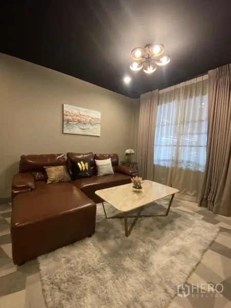 Townhouse for rent in Bang Kapi, Bangkok - Cozy living room with brown leather sectional sofa, marble coffee table and soft rug.