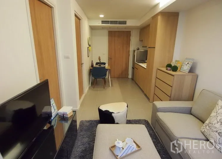 Condominium for rent in Pathum Wan, Bangkok - Open-plan living area with sofa, TV console and dining set beside a wood-finish kitchenette.