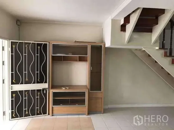 ทาวน์เฮาส์ ให้เช่าในSuan Luang, Bangkok - มุมห้องนั่งเล่นมีบันไดและชั้นวางทีวี ใกล้ประตูเหล็กดัดลวดลาย