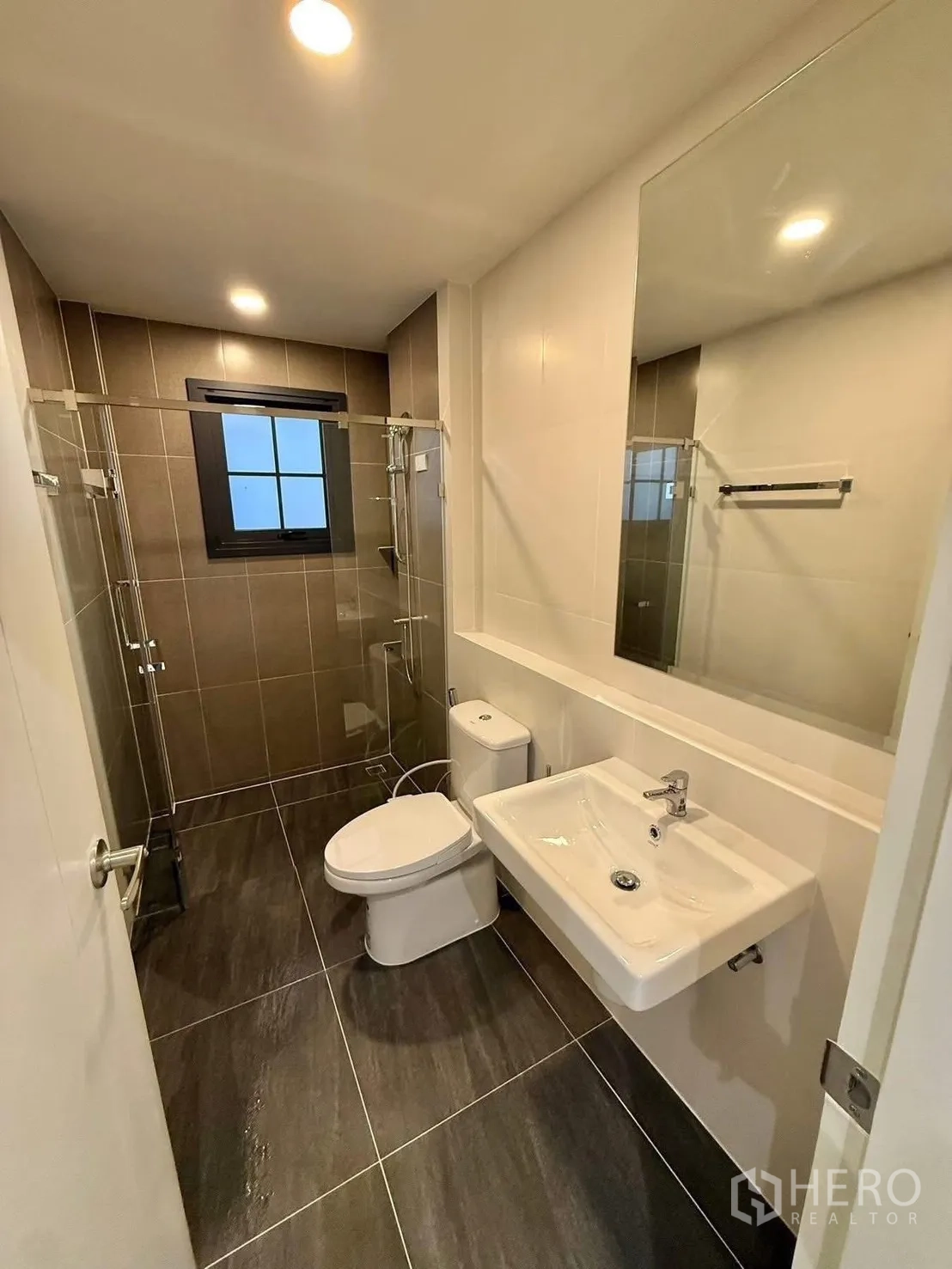 Detached House for rent in Bang Phli, Samut Prakan - Second bathroom with glass shower, white basin and dark floor tiles.