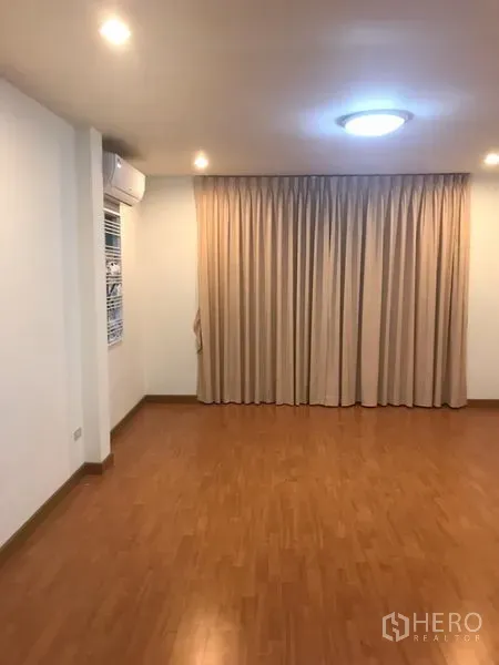 Detached House for rent in Din Daeng, Bangkok - Empty room with laminate wood floor, beige curtains, recessed lights and a wall air conditioner.