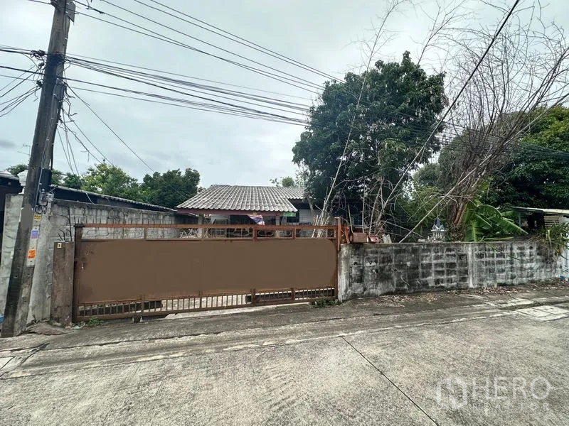 ที่ดิน ขายในPhra Khanong, Bangkok - ประตูเลื่อนโลหะและกำแพงด้านหน้าที่ดิน มีต้นไม้ใหญ่และสาธารณูปโภคให้เห็น