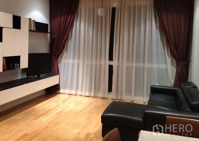 คอนโด ให้เช่าในKhlong Toei, Bangkok - ห้องนั่งเล่นพื้นไม้ ผ้าม่านโปร่งและทึบ ชั้นวางทีวีลอยตัว พร้อมโซฟาหนังสีดำ ในคอนโดคลองเตย