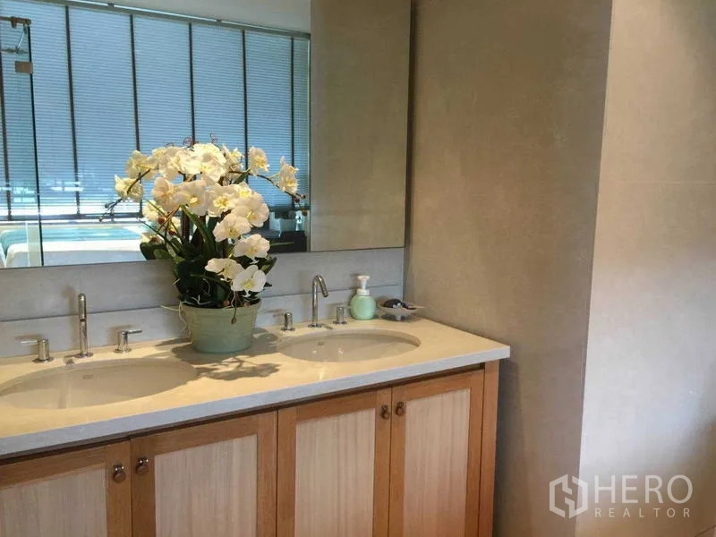 คอนโด ให้เช่า - ห้องน้ำสมัยใหม่พร้อมอ่างล้างหน้าแบบคู่ กระจกบานใหญ่ และตู้ไม้โทนอ่อน ประดับดอกกล้วยไม้