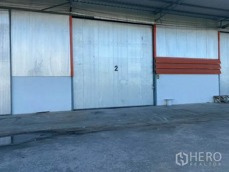 货栈 出租在Mueang Pathum Thani, Pathum Thani - 编号2的大型金属推拉门，连接带顶装卸区与混凝土硬化地面。