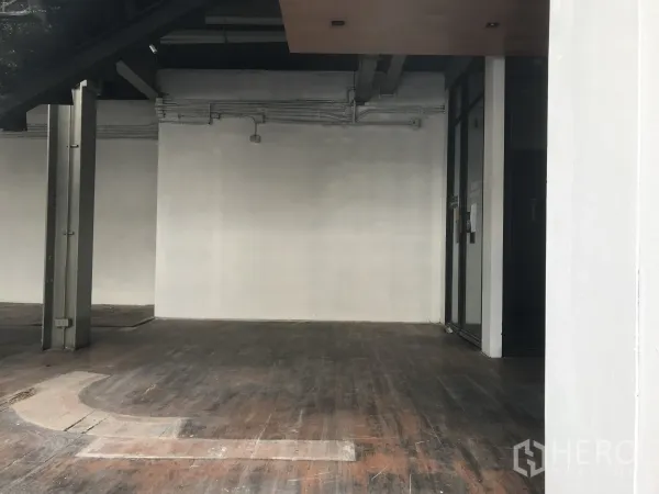 零售空间 出租在Watthana, Bangkok - 空置铺面，白色墙面、外露管线与深色木地板，后方有门