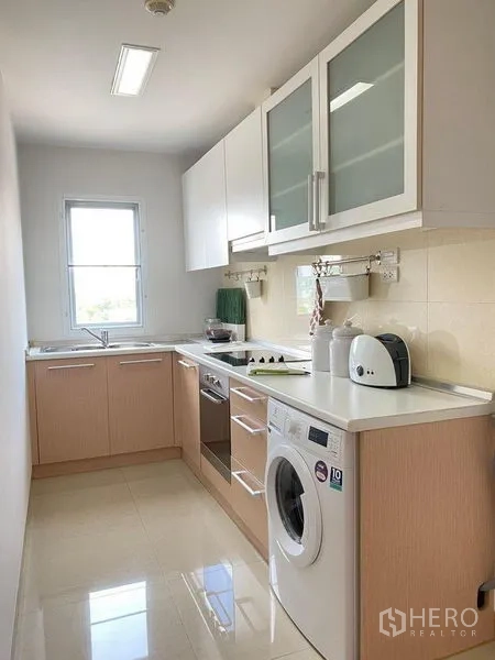 Condominium for sale in Phra Khanong, Bangkok - Galley kitchen with white and wood cabinets, oven, cooktop, sink, and washing machine.