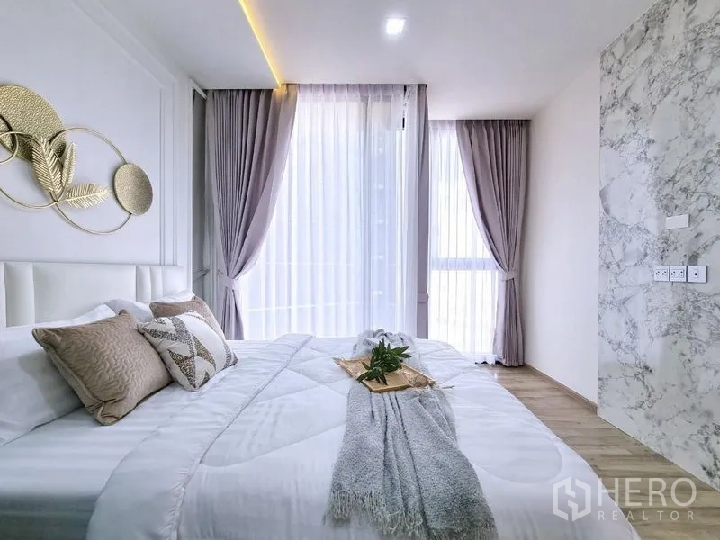 公寓 出售 - 卧室一角，大窗与灰色窗帘，旁有大理石纹墙面。