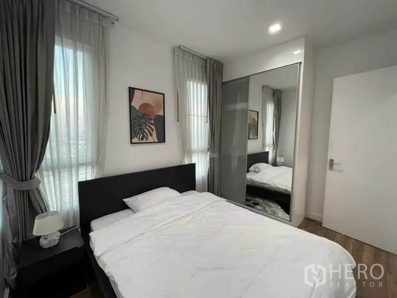 Condominium for rent or sale in Watthana, Bangkok - Bedroom with mirrored sliding wardrobe, bedside table and soft lighting.
