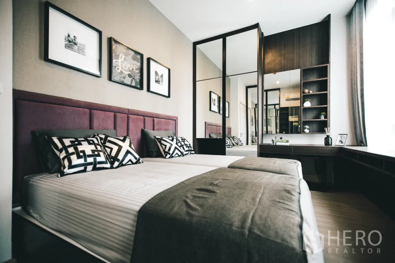 Condominium for rent in Huai Khwang, Bangkok - Primary bedroom with upholstered headboard, mirrored wardrobe, and built-in desk and shelving.