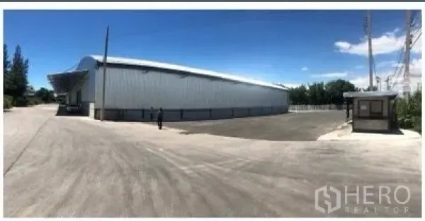 货栈 出租在Chon Buri - 是拉差金属板仓库外观，宽阔卡车回转庭院与门卫岗亭，晴朗天空下。