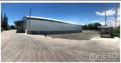 货栈 出租在Chon Buri - 是拉差金属板仓库外观，宽阔卡车回转庭院与门卫岗亭，晴朗天空下。