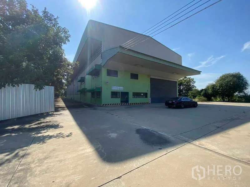 Warehouse for rent in Lat Lum Kaeo, Pathum Thani - Large green warehouse with cantilevered loading canopy, roller shutter and expansive concrete yard under blue sky.
