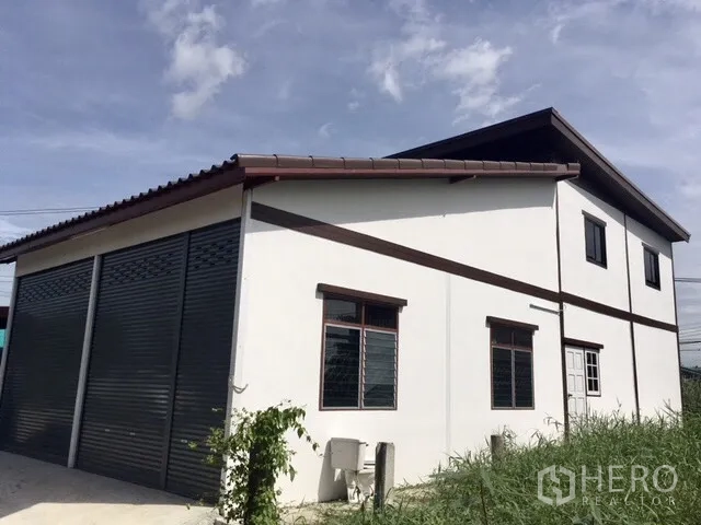 คลังสินค้า ให้เช่าในLam Luk Ka, Pathum Thani - มุมมองด้านข้างและด้านหลังของโกดังสองชั้น มีหน้าต่าง ประตูม้วน และพื้นที่สีเขียวรอบอาคาร.