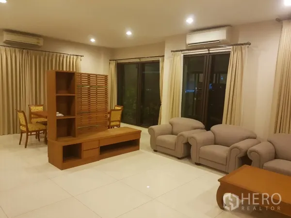 ทาวน์เฮาส์ ให้เช่าในBang Kapi, Bangkok - ห้องนั่งเล่นกว้าง พื้นกระเบื้อง ชุดโซฟาสีเบจ ตู้ทีวีไม้ และประตูกระจกบานเลื่อน