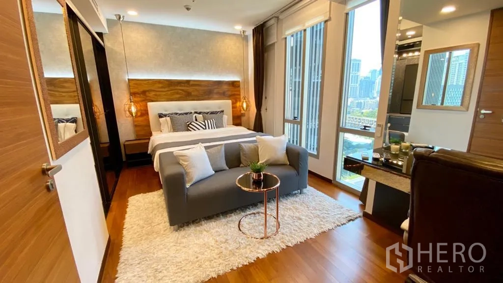 公寓 出售在Khlong Toei, Bangkok - 宽敞卧室，双人床、小沙发、大窗与城市景色。