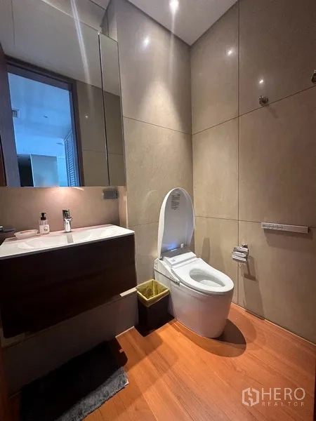 Condominium for rent or sale in Sathon, Bangkok - Modern powder room with wall-hung vanity, toilet, and warm stone tiles.