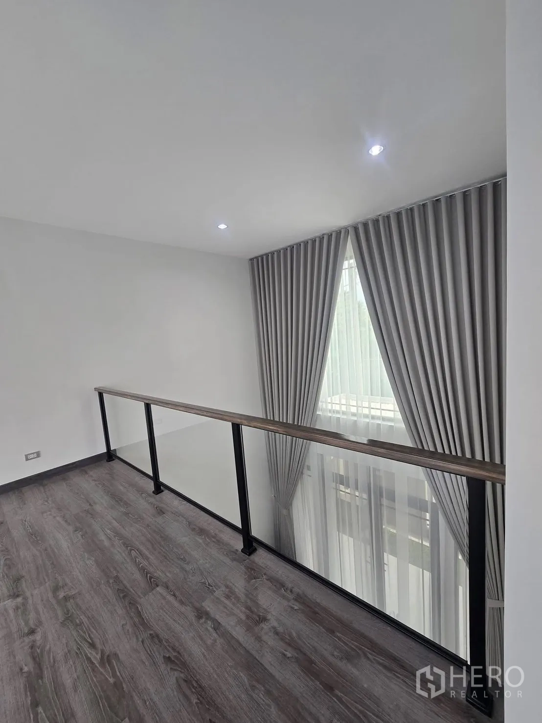 Semi-detached House for rent in Suan Luang, Bangkok - Upper landing with glass railing overlooking a double-height space and tall curtains.