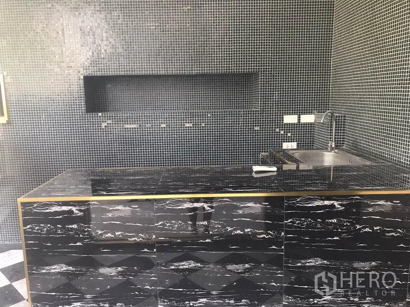 零售空间 出租在Watthana, Bangkok - 内置黑色石材吧台与洗手池，墙面为马赛克瓷砖。