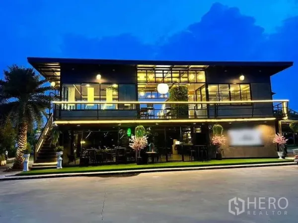 บ้าน ขายในKhlong Luang, Pathum Thani - อาคารกระจกสองชั้นสไตล์โมเดิร์นเปิดไฟยามค่ำ พร้อมระเบียงและที่นั่งกลางแจ้ง