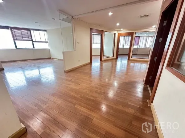 Office Space for rent - Spacious open-plan office with wooden floors, recessed lights and a corner glass partition by windows.