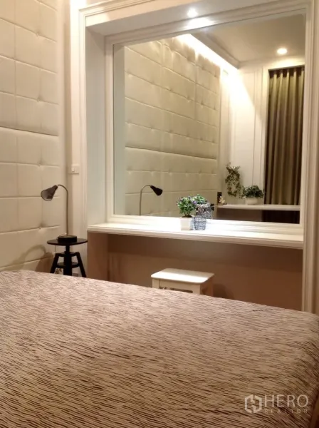 Condominium for rent in Watthana, Bangkok - Bedroom with padded wall panels, a large framed mirror, and a white dressing desk under soft lighting.