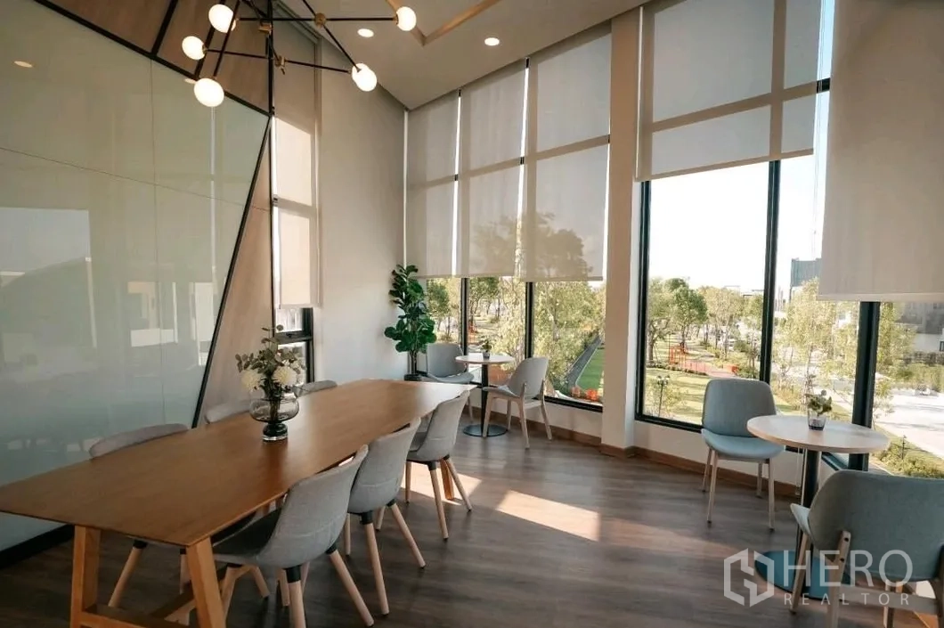Townhouse for rent in Bang Phli, Samut Prakan - Modern clubhouse interior with long wooden table, pendant lights and large windows over greenery.