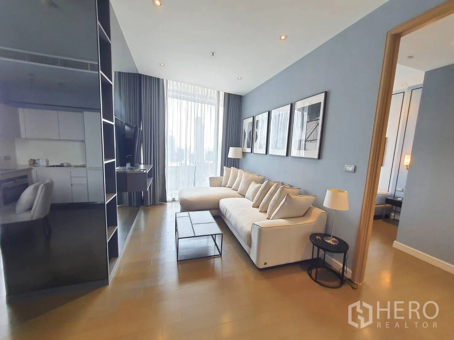 คอนโด for rent in Pathum Wan, Bangkok - พื้นที่นั่งเล่นเปิดโล่ง มีโซฟาขนาดใหญ่ ผ้าม่านสูง ผนังติดทีวี และทางเข้าห้องนอน