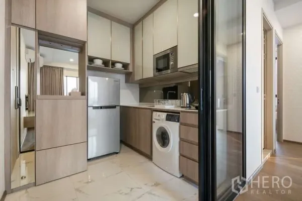 Condominium for rent - Compact built-in kitchen with fridge, microwave, washing machine and ample cabinetry behind a glass partition.