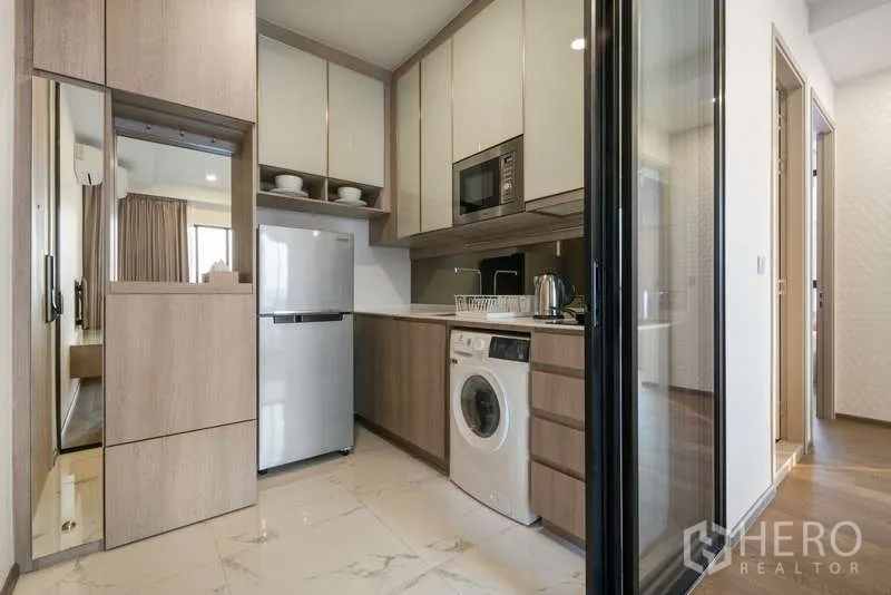 Condominium for rent - Compact built-in kitchen with fridge, microwave, washing machine and ample cabinetry behind a glass partition.