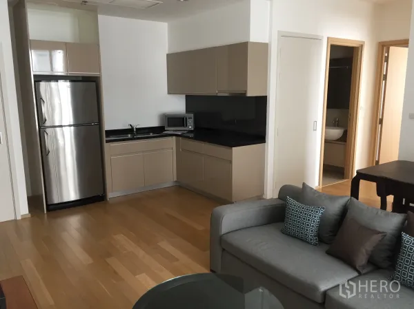 คอนโด ให้เช่าหรือขายในWatthana, Bangkok - ครัวเปิดสไตล์โมเดิร์น พร้อมตู้เย็นสแตนเลส ตู้บิลท์อิน เคาน์เตอร์หินสีดำ พื้นไม้ และโซฟาสีเทาในคอนโดกรุงเทพฯ