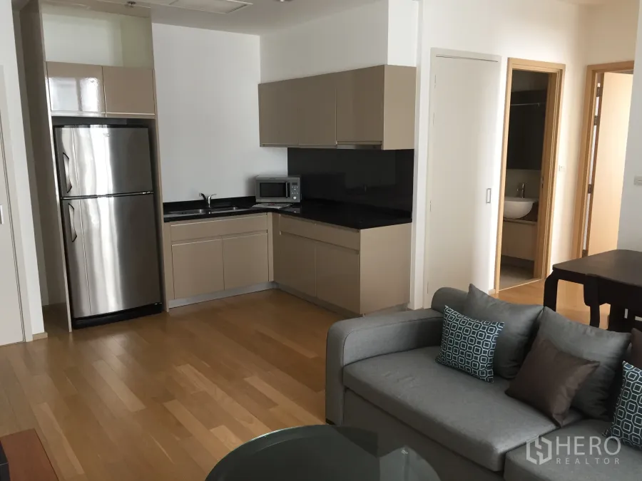 公寓 出租或出售在Watthana, Bangkok - 开放式厨房，米色橱柜与黑色台面，木地板，配不锈钢冰箱与灰色沙发。