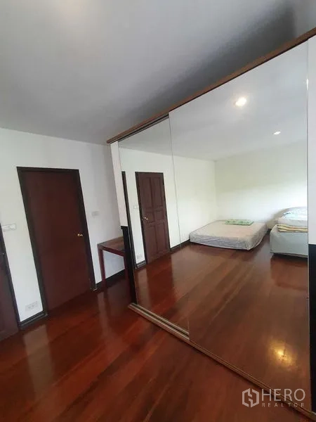 Townhouse for rent or sale in Suan Luang, Bangkok - Bedroom with mirrored wardrobe, polished wood floors and two beds.