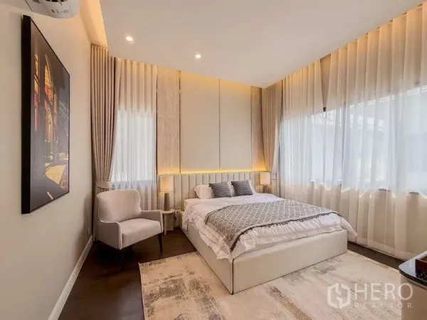 Detached House for rent or sale in Bang Kapi, Bangkok - Bright bedroom with large windows, upholstered bed and bedside lamps.