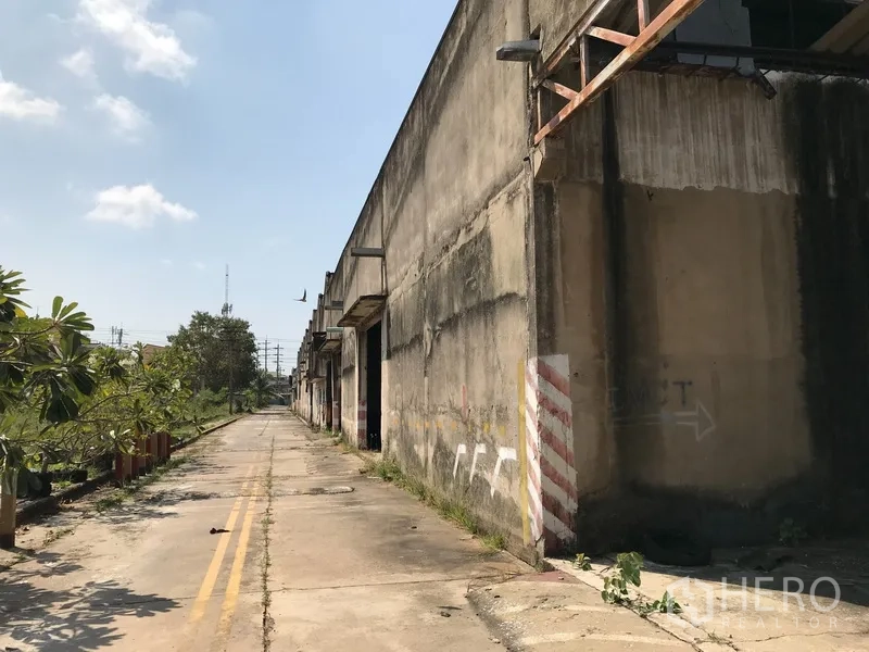 Land for rent in Phra Pradaeng, Samut Prakan - Extended warehouse facade running along a private driveway under a clear sky.