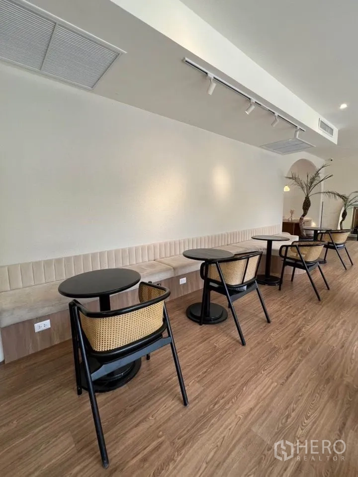 零售空间 出租在Watthana, Bangkok - 一排黑色圆桌与藤编椅沿嵌入式卡座排列，顶部为轨道灯。