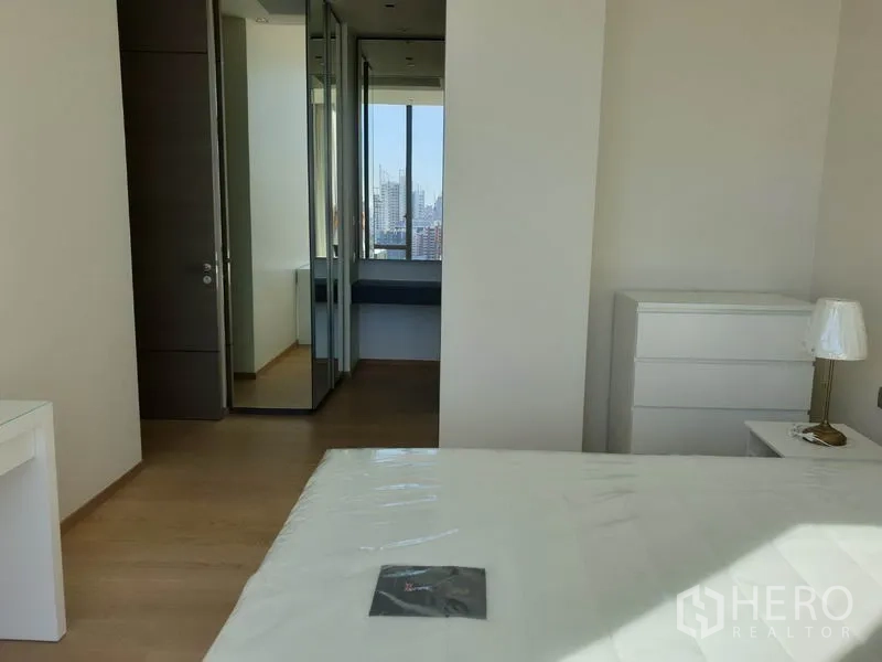 Condominium for rent in Pathum Wan, Bangkok - Master bedroom view toward mirrored wardrobe and dressing area with city view.