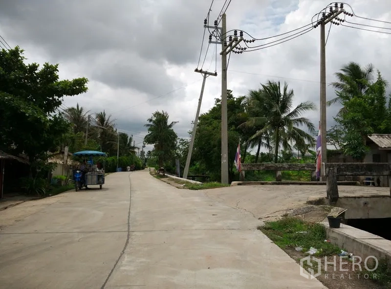 Factory for rent or sale in Krathum Baen, Samut Sakhon - Quiet local road with power lines and a small canal bridge amid lush greenery.