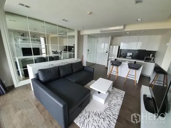 คอนโด ให้เช่าหรือขายในWatthana, Bangkok - ห้องนั่งเล่นแบบเปิดโล่ง โซฟาหนังสีดำ ผนังกระจก และครัวไอแลนด์สีขาว