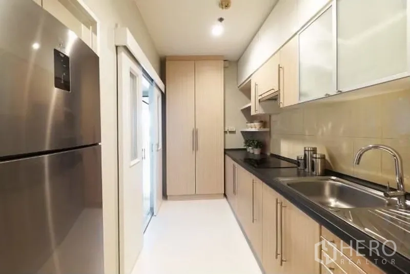 คอนโด ให้เช่าในWatthana, Bangkok - ครัวแบบแกลเลย์สว่างตา ตู้ไม้โทนอ่อน เคาน์เตอร์สีดำ อ่างล้างจานและตู้เย็นสเตนเลส