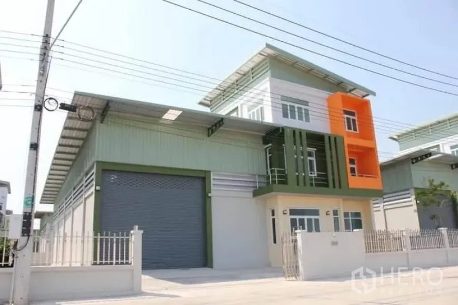 Factory for sale in Lam Luk Ka, Pathum Thani - Modern factory exterior in Lam Luk Ka with a large roller shutter, colorful office block and gated driveway.